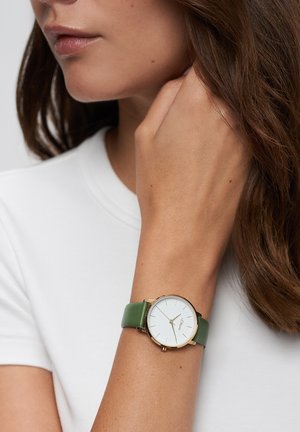 Runde Uhr mit weißem Zifferblatt, goldenen Markierungen und grünem Lederarmband. Die Uhr besticht durch ein minimalistisches Design und polierte Beschläge.