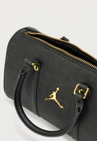 Musta kuvioitu käsilaukku, jossa on kultainen vetoketju ja yksityiskohdat. Varustettu säädettävillä olkahihnoilla ja näkyvällä kultaisella logolla. Sileä pinta, kompakti muoto.