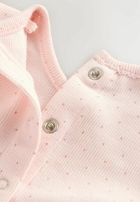 Světle růžová vroubkovaná látka s malým tečkovaným vzorem a stříbrnými lisovacími knoflíky na oblečení pro batolata.