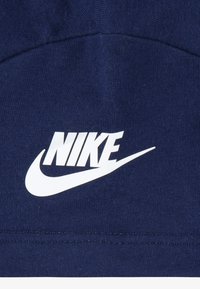 Tummansininen puuvillakangas, jossa on sileä pinta, jonka keskellä on näkyvä valkoinen Nike-logo ja swoosh-kuvio.