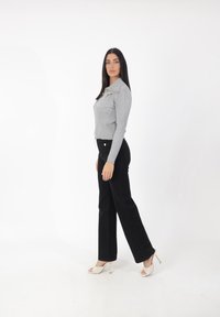Top de manga larga gris acanalado con cierre de cremallera y cuello, combinado con pantalones de campana negros de cintura alta y sandalias de tacón blancas.