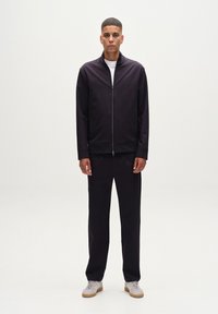 Temno modra zip-up jakna in ujemajoče hlače, narejene iz gladkega materiala. V kombinaciji z svetlosivimi supergami, ki imajo gumijast podplat in vezalke.