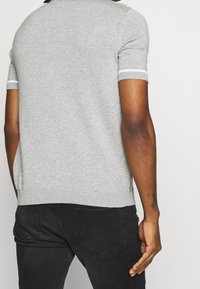 Pull gris à manches courtes en maille avec ourlets côtelés, présentant une texture lisse et des fentes latérales, associé à un jeans foncé.