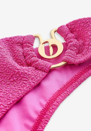 Roze bikini-top met textuurstof en metallic draad, versierd met een goudkleurig cirkelvormig hardware-detail in het midden.
