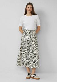 Witte geribbelde top met korte mouwen gecombineerd met een midi-rok met een zwart en beige luipaardprint, aangevuld met zwart en beige sneakers.