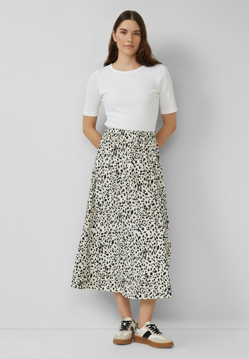 Witte geribbelde top met korte mouwen gecombineerd met een midi-rok met een zwart en beige luipaardprint, aangevuld met zwart en beige sneakers.