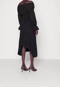 Haut noir décolleté avec des manches bouffantes et une taille froncée, associé à une jupe noire fluide avec un ourlet asymétrique et des sandales à enfiler.