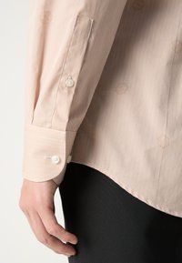 Gestreiftes Langarmhemd in zartem Rosa mit dezenten gestickten Akzenten. Verfügt über einen abgerundeten Manschetten und Knöpfe und präsentiert sich aus einem leichten, strukturierten Stoff.