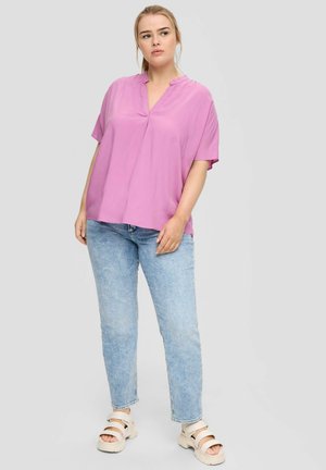 Blouse rose à manches courtes avec un décolleté en V, fabriquée à partir d'un tissu lisse. Portée avec un jean bleu clair et des sandales beiges. Design simple, coupe décontractée.