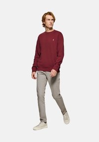 Burgundyk sweatshirt med rund halsringning, ribbade mudd och nederkant; matchad med ljusgrå byxor och vita sneakers, bärs av en person som går.