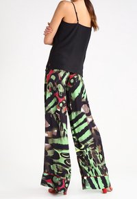 Czarny top bez rękawów połączony z szerokimi spodniami w zielone, czarne i czerwone abstrakcyjne wzory. Gładki materiał z wyrazistymi detalami.