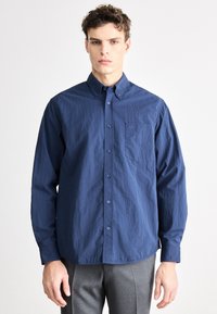 Cămașă bleumarin cu mâneci lungi și nasturi, dintr-un material moale și texturat, cu un buzunar la piept și un mic logo pe zona buzunarului.