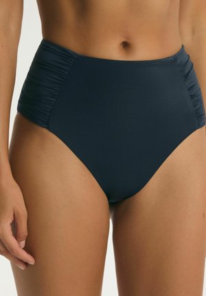 Plavkové nohavičky s vysokým pásom v tmavomodrej farbe s nariasenými stranami, nosené osobou so stredným tónom pokožky, zobrazené od pásu po hornú časť stehien.