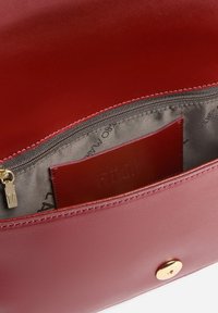 Interno di una borsa in pelle rossa con tasca con zip e portacarte. La fodera è grigia con marchio impresso. Dotata di finiture in oro.