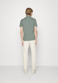 Polo vert à manches courtes avec une coupe droite, un col et des détails de couture subtils, associé à un pantalon slim beige et des chaussures blanches.