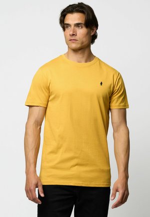 Yellow cotton T-shirt with a round neck, short sleeves, and a small black logo on the chest, paired with black pants.