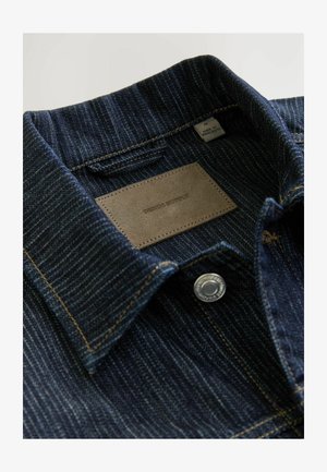 Teksasest meenutav särk, millel on tume sinine, tekstuuriga kangas, krae, nahkalgus "DENIM SUPPLY" ja hõbedane snaps-nupp.