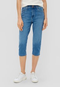 Jeans capri en denim bleu avec une taille mi-haute, un ourlet fini et une légère décoloration. Associés à des sneakers blanches pour un look décontracté.