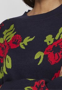 Pull bleu marine avec un motif floral rouge et vert. Présente un col rond et des poignets côtelés. Texture en maille douce.
