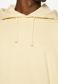 Sudadera ligera amarilla de textura suave, con bolsillo canguro, cordones y un pequeño logo bordado de "Levi's" en el pecho.