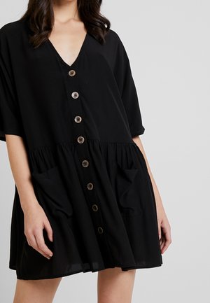 Black short-sleeve dress features a V-neck, button front with contrasting buttons, gathered waist, and two side pockets. Smooth fabric texture.