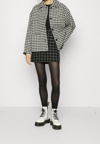 Czarna i biała kurtka w wzór houndstooth w oversize'owym kroju, dopasowany czarny top, w kratkę mini spódniczka, czarne rajstopy i białe sznurowane botki.