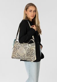 Handtas met een ingewikkeld metallic patroon, kleur room en goud, textuur oppervlak, handvat aan de bovenkant en verstelbare schouderband.