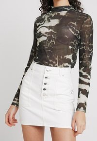 Långärmad, genomskinlig topp med ett svartvitt abstrakt mönster, kombinerad med en vit denim mini-skjorta med knappstängning framtill och fickor.