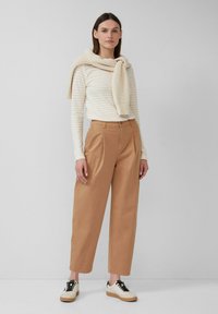 Camicia a righe beige a maniche lunghe abbinata a pantaloni beige a vita alta e sneakers bianche con lacci neri e suola beige, maglione a maglia testurizzata appoggiato.
