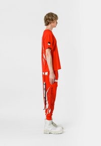 Camiseta roja de gran tamaño y pantalones sudadera con diseño de alas blancas, con acentos texturizados. Combinado con botas blancas y bolsillos cargo laterales.