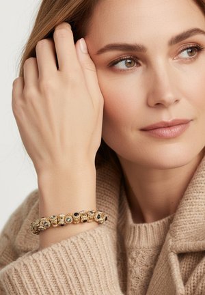 Gouden armband met fijn kralenwerk met zwarte en groene accenten, gedragen aan een hand tegen een zachte, beige gebreide trui.