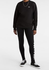 Svart crewneck-tröja med Vans-logga, tillsammans med svarta leggings med vit sidologga. Skor: svarta sneakers med vita snören.