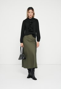 Black blouse with ruffled collar, long sleeves; green satin skirt, ankle length; black knee-high boots; black handbag with curved handles.