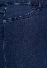 Mörkblå jeans i denim med en slät yta, en framficka med en mässingsknapp och detaljerad sömnad längs sömmarna.