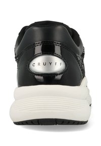 Schwarzer Sneaker mit glänzender Oberfläche, atmungsaktivem Obermaterial aus Mesh, weißer Zwischensohle und Gummilaufsohle. Verfügt über ein kreisförmiges silbernes Akzent mit "CRUYFF"-Branding.