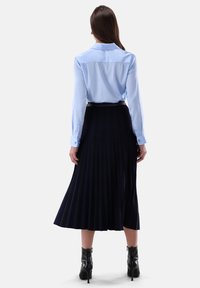 Hellblaues langärmliges Hemd mit Kragen, kombiniert mit einem dunkelblauen Faltenrock. Schwarze hohe Stiefeletten runden das Outfit ab.