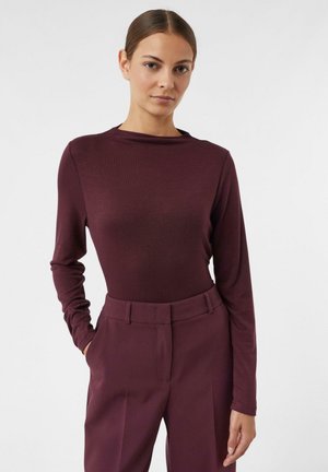 Maglietta a maniche lunghe in tessuto bordeaux scuro con scollo rotondo e vestibilità aderente, abbinata a pantaloni a vita alta bordeaux sartoriali.