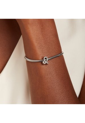Silver metal bracelet with a flexible design, featuring a small charm with a swirl pattern. Smooth texture against brown skin.