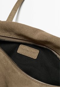 Interno di borsa in suede marrone con fodera nera, dotata di zip e etichetta impressa "Massimo Dutti." Superficie texturizzata e design semplice.