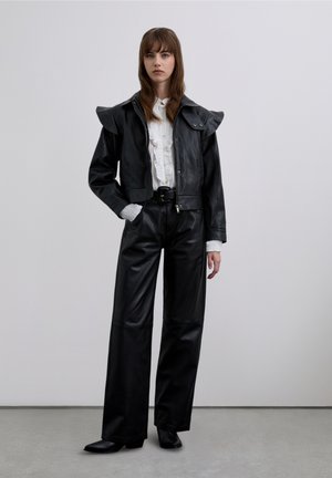 Chaqueta de cuero negra con hombros fruncidos, cierre de cremallera y gran cuello, combinada con pantalones de cuero negros de talle alto.