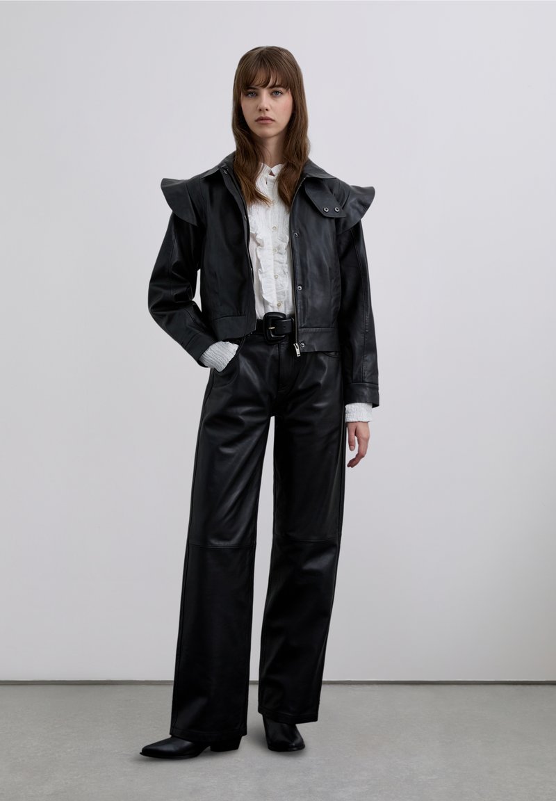 Sort læderjakke med rynkede skuldre, lynlåslukning og stor krave kombineret med sorte læderbukser med høj talje.