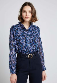 Chemisier à manches longues et boutonné, de couleur bleu marine, avec un motif floral dans des tons de bleu et de violet, doté d'un col et de poignets à volants.