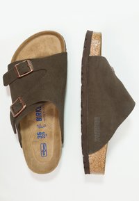 Brown suede sandals with two adjustable metal buckles, contoured cork footbed, and textured brown rubber sole.
