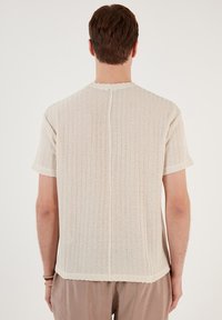 Beżowa t-shirt z prążkowanej bawełny, z krótkimi rękawami, lekko teksturowana, z okrągłym dekoltem i prostym dołem, widoczna z tyłu.