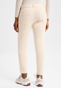 Beige corduroy broek met een slim fit, voorzien van achterzakken en een gestructureerd oppervlak, gecombineerd met chunky witte sneakers met roze zolen.