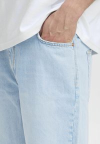 Jeans de denim azul claro con un ajuste relajado, que presentan detalles de costura, bolsillos laterales y una textura ligeramente desgastada.