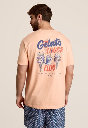 T-shirt en coton pêche avec un design graphique featuring des cornets de glace et le texte "Gelato Lover Club" en bleu et rouge. Manches courtes.