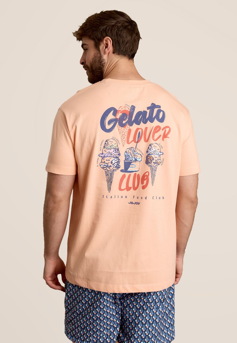 Perzikkleurig katoen T-shirt met een grafisch ontwerp van ijsjes en de tekst "Gelato Lover Club" in blauw en rood. Korte mouwen.
