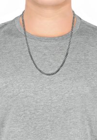 Sølv kæderekæde med sammenflettede led, hængende over en lysegrå crew-neck t-shirt; glat tekstur, moderat tykkelse og klassisk design.