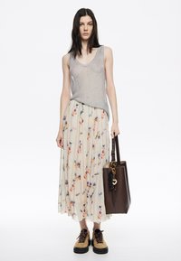 Top sin mangas de color gris claro y una falda fluida color crema con estampados florales; bolso tote marrón con un llavero; zapatos beige con suela negra.